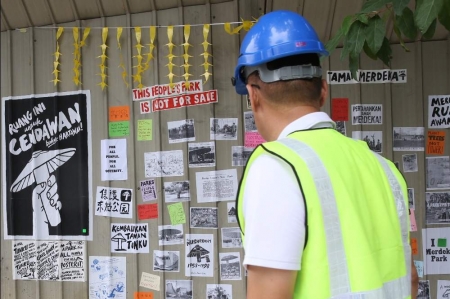 A man looks at the striking poster of a raised fist grabbing a mushroom on a poster-covered wall, with the slogan ‘Ruang ini untuk cendawan, bukan hartawan’ (This space is for mushrooms, not property tycoons).